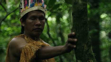 Portrait-of-an-indigenous-guy-wearing-a-feathered-hat-and-fringed-shirt-in-the-dense-forest-in-Leticia,-Amazon,-Colombia