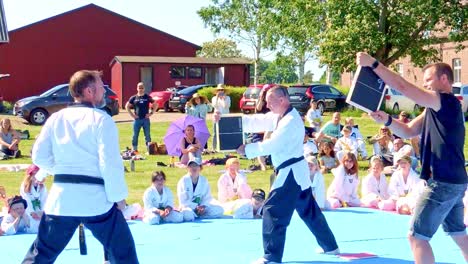 El-Instructor-Y-El-Estudiante-De-Taekwondo-Están-Rompiendo-Un-Trozo-De-Madera-Con-Una-Patada.