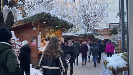 Christmas-markets-with-tourists-passing-by,-snowy-winter-cold-atmosphere,-day