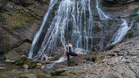 Vista-Trasera-De-Una-Joven-En-Forma-Practicando-Yoga-En-Un-Paisaje-De-Cascada,-Plano-General