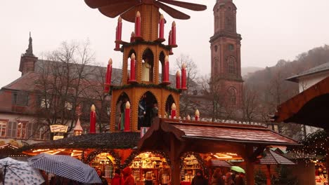 Holzpyramide-Mit-Rotierenden-Propellern-Vor-Einem-Kirchturm-In-Heidelberg,-Deutschland,-Auf-Einem-Festlichen-Weihnachtsmarkt-In-Europa