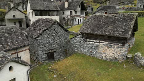 Aerial-drone-forward-moving-shot-flying-over-old-empty-village-houses-along-the-slope-in-Cavergno,-District-of-Vallemaggia,-Canton-of-Ticino-in-Switzerland