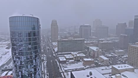 Snowy-aerial-past-Hyatt-Regency-building-with-view-down-South-Temple-Street,-SLC