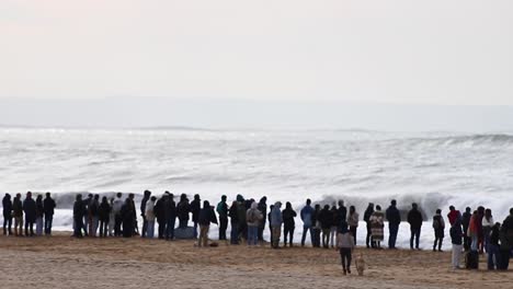 People-gathering-on-a-beach-to-watch-big-waves-rolling-and-crashing-onto-the-shore