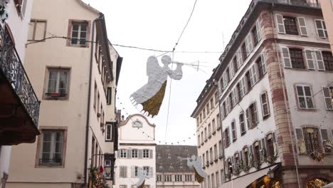 Christmas-angel-decorations-hanging-over-european-streets-of-Strasbourg,-France-at-a-Festive-Christmas-market-in-Europe