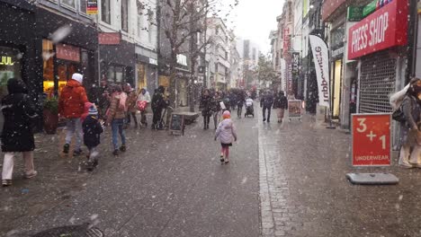 People-walking-in-the-city-shopping-street-during-cold-and-snowy-wintertime---Hasselt,-Belgium