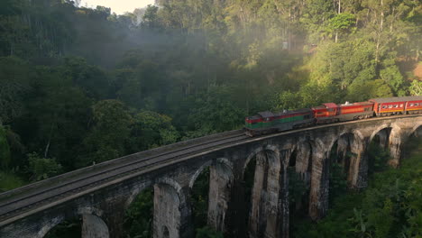 Toma-Aérea-De-Retroceso-De-Un-Tren-Diésel-Cruzando-El-Puente-De-9-Arcos-En-Un-Tren-Nocturno-Brumoso-Por-La-Mañana