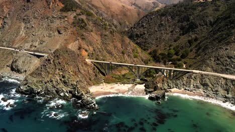 Capture-Una-Perspectiva-Aérea-Cinematográfica-Y-Panorámica-De-Big-Sur,-Centrándose-En-Mostrar-El-Puente-Bixby-Creek-Y-La-Carretera-Panorámica.