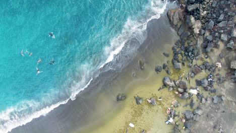 People-swim-by-Papakolea-Beach-in-Hawaii,-spinning-overhead-aerial