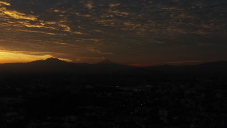 Aerial-view-of-Mexico-City's-skyline-under-the-twilight-with-the-silhouettes-of-Popocatépetl-and-Iztaccíhuatl-volcanoes-looming