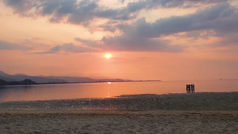 Time-lapse-during-beautiful-sunset-over-ocean-water-beach-with-crowds-of-people-and-moving-clouds-in-sky,-capital-city-of-Dili,-Timor-Leste,-Southeast-Asia