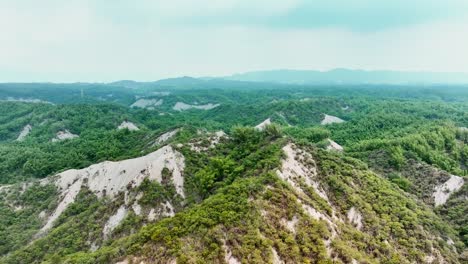SLow-forward-flight-over-greened-badlands-with-moonscape-during-cloudy-day---Taiwan,-Tianliao,-Kaohsiung
