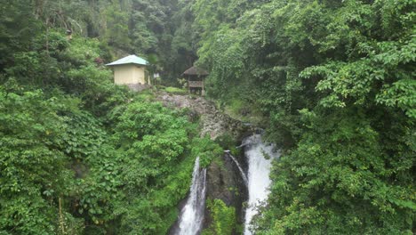 Waterfalls-and-huts-surrounded-by-jungle-environment-on-a-cliff-in-Bali,-Indonesia
