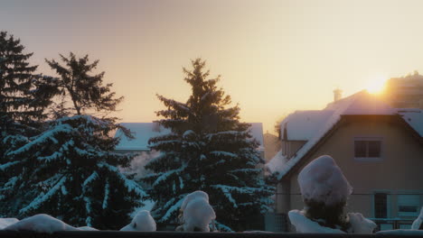 Filmischer-Zeitraffer-Eines-Sonnenaufgangs-Während-Eines-Kalten,-Verschneiten-Winters-Mit-Häusern-Mit-Schornsteinrauch-Und-Bäumen-Im-Hintergrund