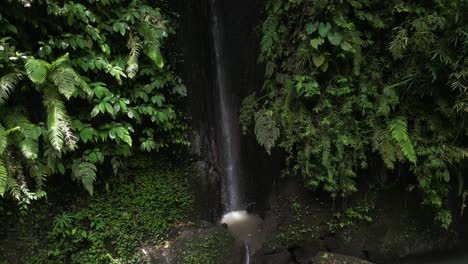 A-small,-trickling-waterfall-surrounded-by-jungle-leaves-and-a-river-in-Bali,-Indonesia