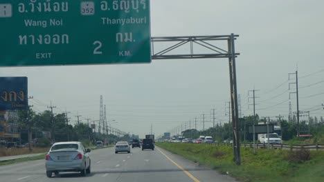 Car-windshield-washer-fluid-spraying-while-the-wiper-moves-to-clean-dust-and-some-debris-as-the-road-leads-to-Wang-Noi-and-Thanyaburi,-Mittraphap-Road,-Thailand