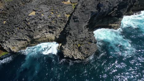 Crashing-waves-against-the-cliffs-on-Nusa-Penida-island-near-to-Bali,-Indonesia-in-the-summer,-aerial