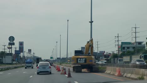 Driving-through-a-construction-on-the-fast-lane-as-a-CAT-backhoe-is-operating,-Mittraphap-Road,-Thailand