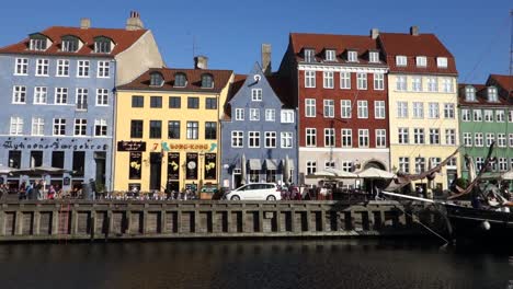 Panning-shot-of-Nyhavn-promenade-and-famoust-waterfront-with-historic-vessel-in-Copenhagen,-Denmark-in-sunny-day