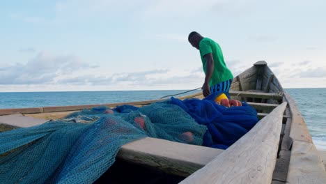 Afrikanischer-Fischer,-Der-An-Einem-Holzboot-Arbeitet-Und-Ein-Netz-Für-Den-Fischfang-An-Der-Tropischen-Westküste-Afrikas-Vorbereitet