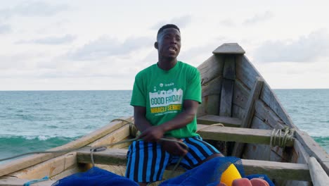 black-male-african-fisherman-working-on-a-wooden-boat-preparing-net-for-fishing-in-tropical-west-coast-of-africa