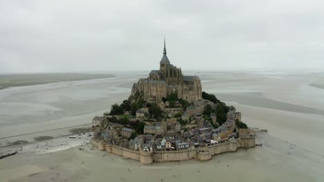 Cámara-Drone-Mont-Saint-Michel-Que-Va-Hacia-El-Castillo,-De-Poca-Altura,-Hay-Muchos-árboles-Alrededor-De-Los-Edificios