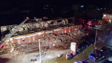 Drone-shot-of-a-motel-building-that-was-badly-burned-being-extinguished-by-the-local-fire-department-using-a-crane-at-night