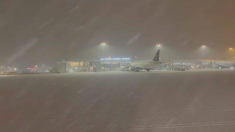Airplane-window-view-landing-under-heavy-snow-storm-with-planes-parked-at-Tromso-airport,-Norway