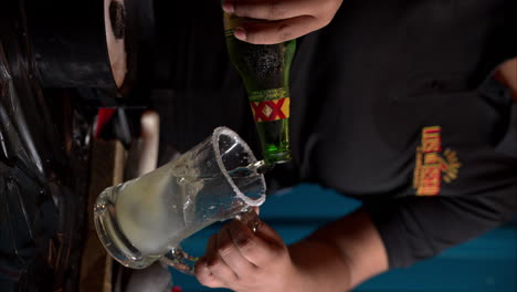 Slow-motion-vertical-close-up-of-a-man-pouring-a-XX-lager-beer-into-a-glass-with-lime-juice-and-salt-preparing-a-michelada-at-a-restaurant-in-Mexico