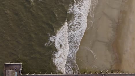 Drone-of-an-empty-beach-in-Tybee-Island-passing-over-pier-with-waves-crashing-and-birds-flying