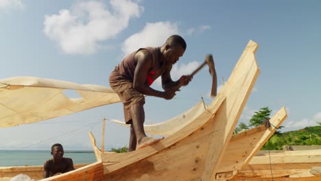 Black-african-man-carving-wooden-fishing-boat-with-adze-on-sea-beach