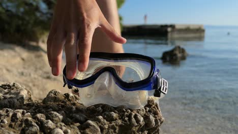 Man-grabbing-snorkeling-mask-on-beach,-child-jumping-in-sea-water-in-background