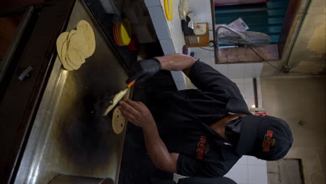 Vertical-slow-motion-of-a-cook-wearing-black-gloves-making-a-quesadilla-with-grilled-cheese-on-a-griddle-at-a-mexican-restaurant
