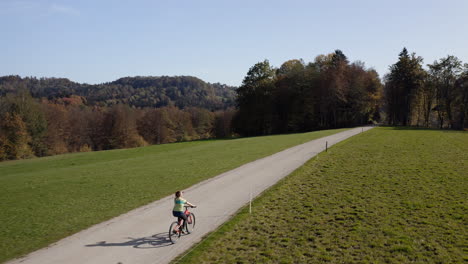 Female-cyclist-riding-on-a-countryside-road-enjoying-autumn-scenery,-aerial-shot