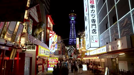 Busy-shopping-street-Shinsekai-and-the-Tsutenkaku-Tower-at-night,-colorful-lights,-and-shops