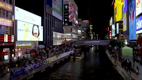 The-Dotonbori-bridge-and-canal-at-night-time,-with-people-walking-around-the-busy-streets-with-billboards