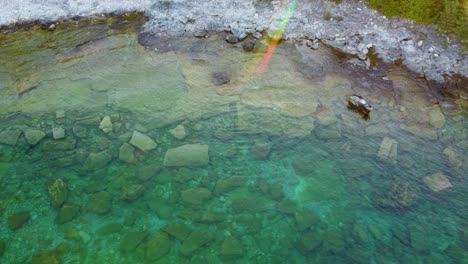 Drone-view-of-a-shallow,-rocky-pool-of-water-with-a-light-leak-effect-on-the-edge