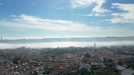 Aerial-orbit-shot-of-mist-over-the-Tagus-River-on-a-sunny-day-with-the-Christ-the-King-statue-and-the-25th-of-April-Bridge-in-Lisbon
