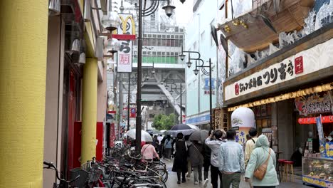 Menschen,-Die-Durch-Die-Straßen-Von-Shinsekai-Laufen,-Mit-Dem-Tsutenkaku-Turm-Im-Hintergrund
