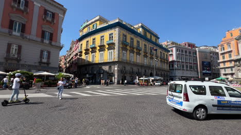 Stadtplatz-Mit-Geschäftigem-Treiben,-Fahrzeugen-Und-Fußgängern,-Sonniges-Ambiente-–-Neapel