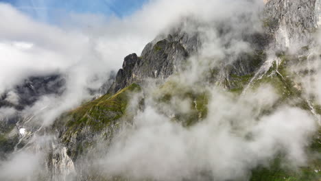 Beautiful-slow-moving-drone-shot-of-rocky-mountain-side-in-Austrian-Alps-through-misty-clouds