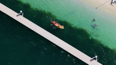 Tourist-couple-paddles-kayak-across-crystal-clear-blue-Caribbean-water-at-resort,-aerial-of-Santa-Barbara-beach