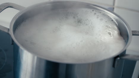 Close-up-of-Boiling-Water-with-Pasta-in-a-big-steel-Pot-on-the-Stove-bubbling-and-steaming-in-slow-motion