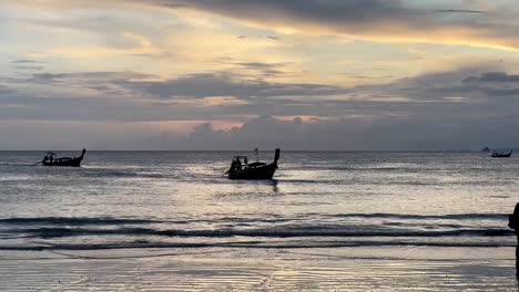Boats-approaching-the-shore-at-sunset,-preparing-to-anchor-and-bring-people-ashore