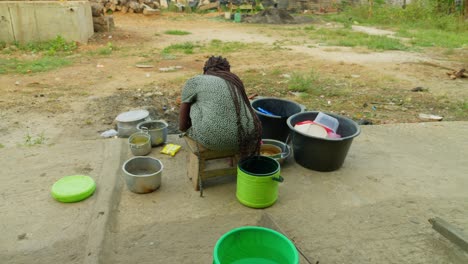 Taken-from-behind-of-a-woman-washing-some-dishes-in-front-of-her-house-in-a-neighborhood-in-Kumasi,-Ghana,-Africa