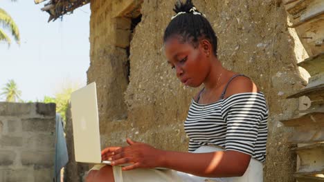 Joven-Negra-Trabajando-En-Su-Moderna-Computadora-Portátil-Mientras-Está-Sentada-En-Una-Remota-Aldea-En-África,-Concepto-De-Tecnología-Mezclado-Con-Estilo-De-Vida-En-Un-País-Pobre-De-África