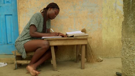 Reading-and-writing,-a-local-girl-is-trying-to-gain-some-basic-education-to-help-bridge-the-gender-gap-in-the-village-of-Kumasi-in-Ghana,-Africa