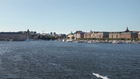 Drone-shot-flying-over-body-of-water-toward-Nybrokajen-and-Strandvägen-in-Stockholm,-Sweden-during-sunny-evening