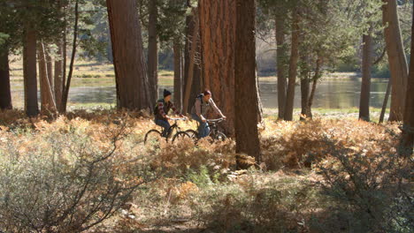 Couple-talking-as-they-ride-mountain-bikes-slowly-in-forest