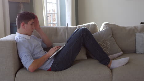 Teenage-Boy-Sitting-On-Sofa-Using-Laptop-At-Home-Shot-On-R3D